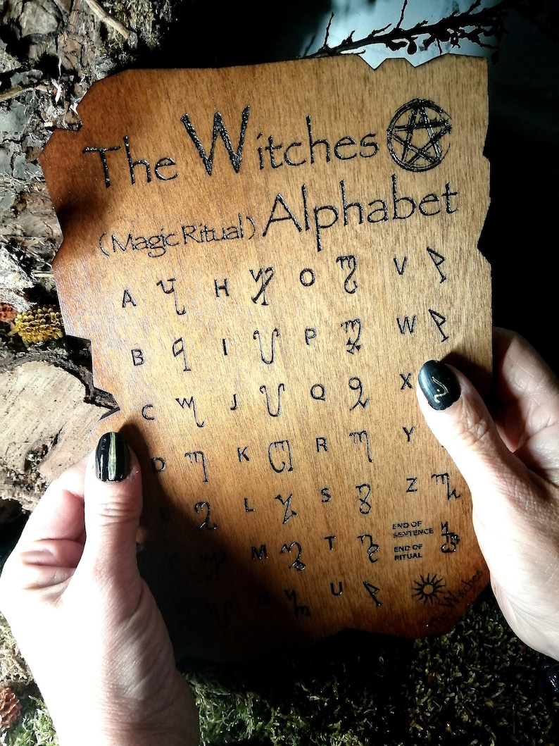 Puede incluir: Una tabla de madera con un pentagrama y el texto "The Witches (Magic Ritual) Alphabet" y un conjunto de s&iacute;mbolos que representan las letras del alfabeto.