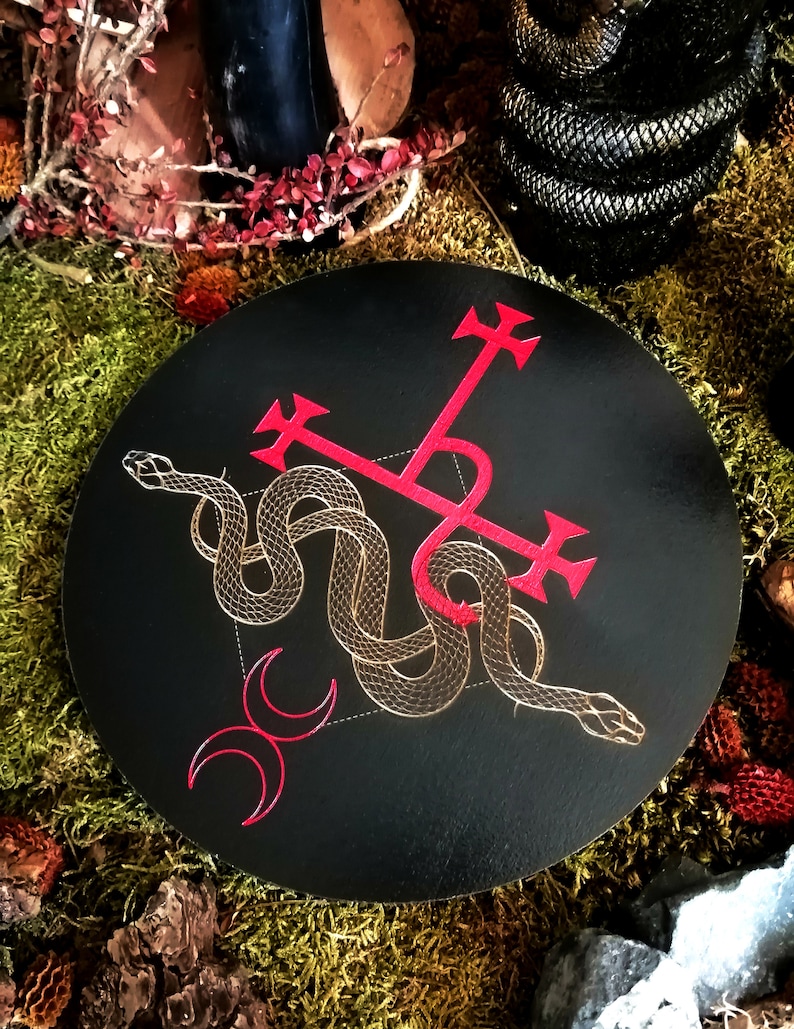 May include: A black circular coaster with a red cross and a gold snake design. The snake is intertwined with the cross and the design is on a black background.