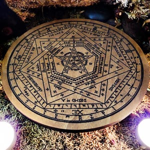 May include: A wooden circle with a pentagram and other symbols inscribed on it. The circle is surrounded by a ring of numbers and letters. The circle is on a bed of moss and other natural materials.