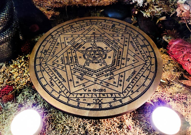 May include: A wooden circle with a pentagram and other symbols inscribed on it. The circle is surrounded by a ring of numbers and letters. The circle is on a bed of moss and other natural materials.