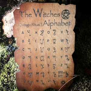 Puede incluir: Una placa de madera con fondo marr&oacute;n y texto negro. El texto dice "The Witches (Magic Ritual) Alphabet" e incluye un s&iacute;mbolo de pentagrama. La placa presenta una cuadr&iacute;cula de letras con s&iacute;mbolos correspondientes.