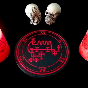 以下が含まれることがあります： 赤い印章と「M A W」という文字が縁に書かれた黒い円。円の上に、両手で目を覆った白い頭蓋骨が2つある。円の両側に赤いろうそくが2本ある。