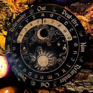 May include: A black wooden Ouija board with gold lettering and symbols. The board features a crescent moon, a sun, and swirling clouds. The text on the board reads "Oui", "Peut-&ecirc;tre", "Non", and "Reformuler".