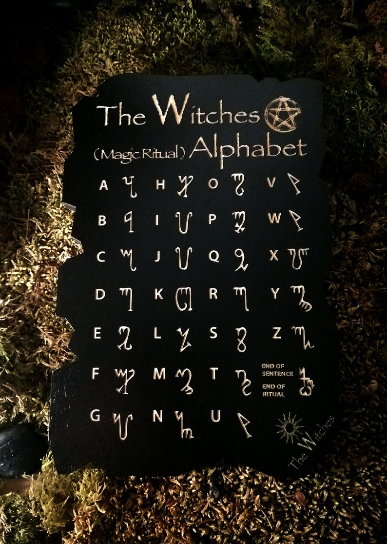 May include: Black wooden board with a gold pentagram and the text "The Witches (Magic Ritual) Alphabet". The board features a gold alphabet with symbols for each letter.