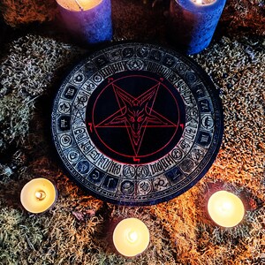 May include: A black wooden circle with a red pentagram and a goat's head inside. The circle is surrounded by a ring of symbols and numbers. The circle is on a bed of moss with three lit candles.