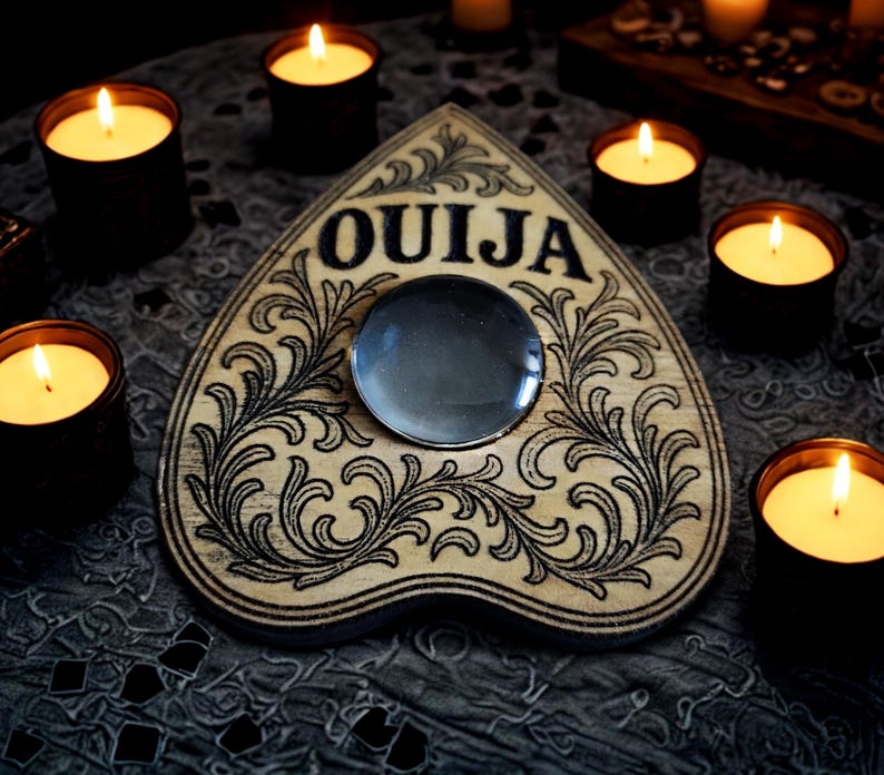 May include: A wooden Ouija board with the word "OUIJA" in black lettering, surrounded by ornate black floral designs. A glass planchette sits in the center. Lit candles in black containers surround the board, creating a mystical ambiance.