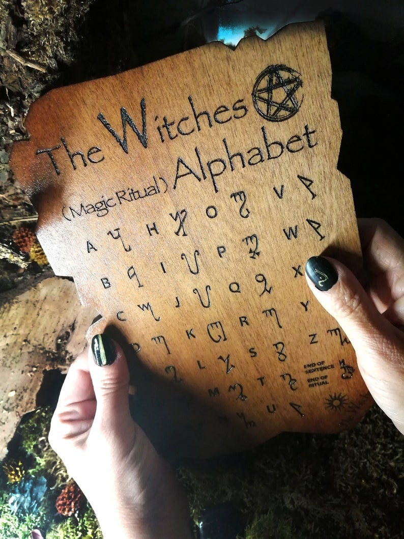 Puede incluir: Una tabla de madera con un pentagrama y el texto "The Witches (Magic Ritual) Alphabet" y una cuadr&iacute;cula de letras en una fuente &uacute;nica.