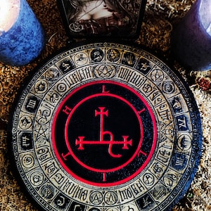 May include: A black and red circular wooden board with a gold-colored border. The board features a black circle with a red border and a red symbol inside. The symbol is a cross with a curved line at the bottom. The board is surrounded by a gold-colored border with various symbols and numbers.