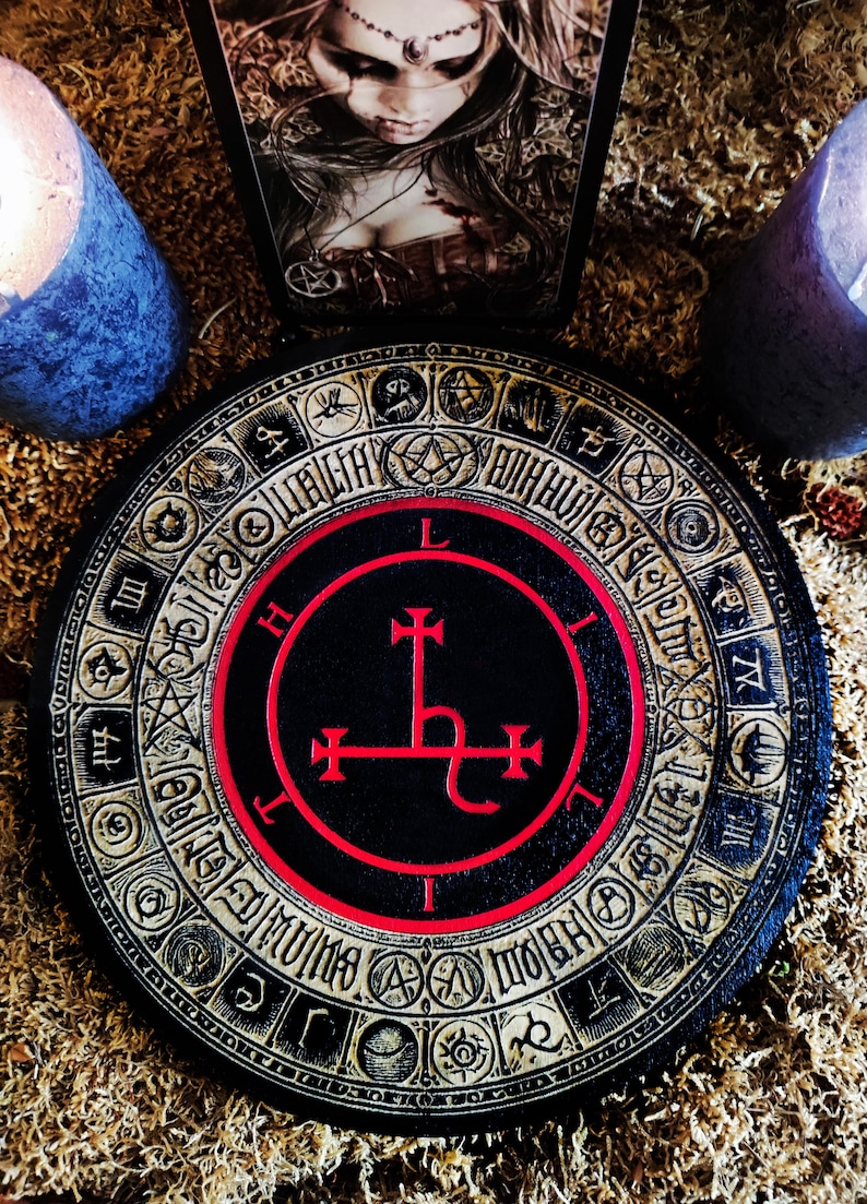 May include: A black and red circular wooden board with a gold-colored border. The board features a black circle with a red border and a red symbol inside. The symbol is a cross with a curved line at the bottom. The board is surrounded by a gold-colored border with various symbols and numbers.