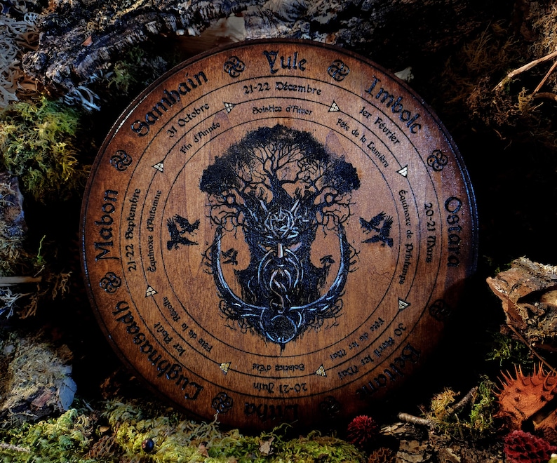 May include: A wooden wheel with a tree of life design and the names of the eight sabbats of the Wheel of the Year in French and English. The sabbats are: Samhain, Mabon, Lughnasadh, Litha, Beltane, Ostara, Imbolc, and Yule.