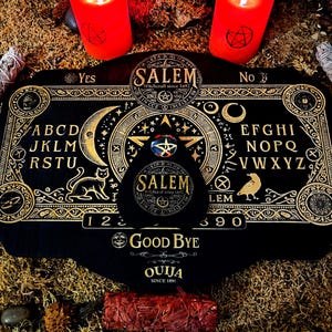 May include: A black Ouija board with gold accents and lettering. The board features a planchette, a pointer, and the letters of the alphabet, numbers, and the words "Yes", "No", and "Good Bye". The board is surrounded by candles and sage.