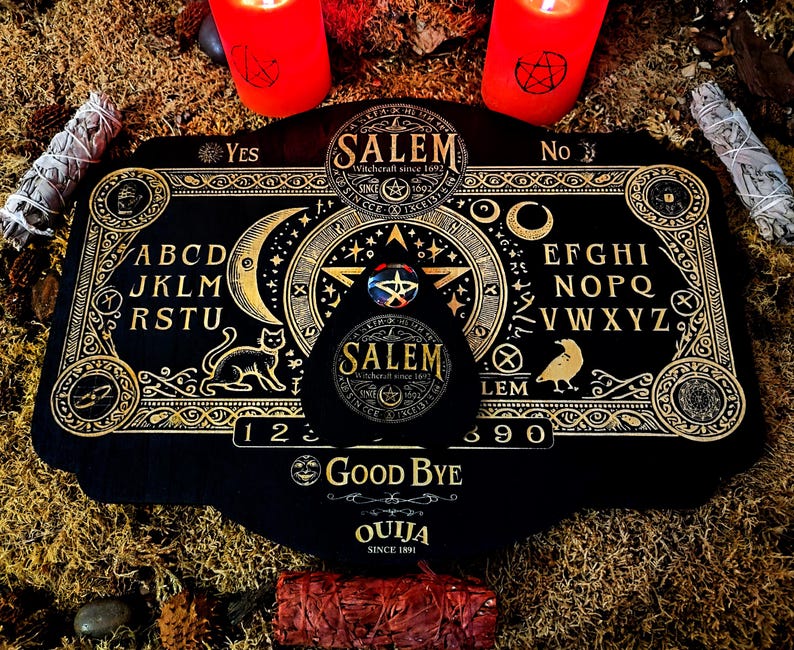 May include: A black Ouija board with gold accents and lettering. The board features a planchette, a pointer, and the letters of the alphabet, numbers, and the words "Yes", "No", and "Good Bye". The board is surrounded by candles and sage.