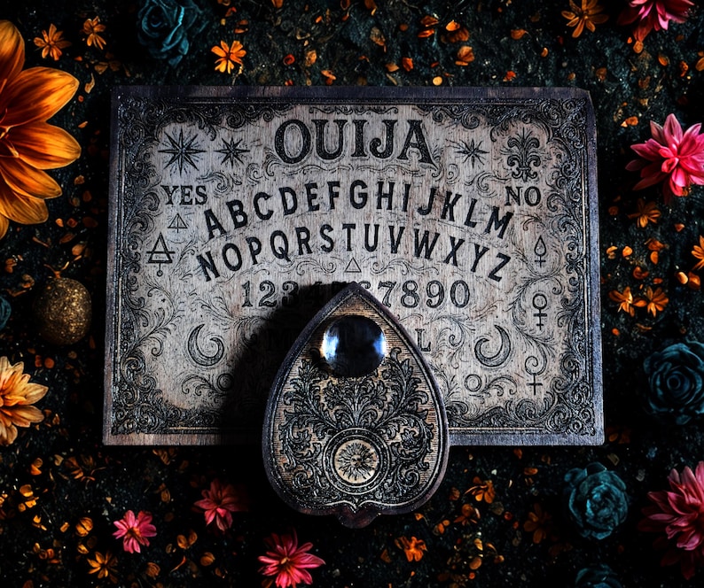 May include: A vintage Ouija board with a planchette, featuring the alphabet, numbers, and the words "Yes" and "No." The board is a light color with dark etched details and ornate borders. The planchette is heart-shaped with a dark, reflective center.