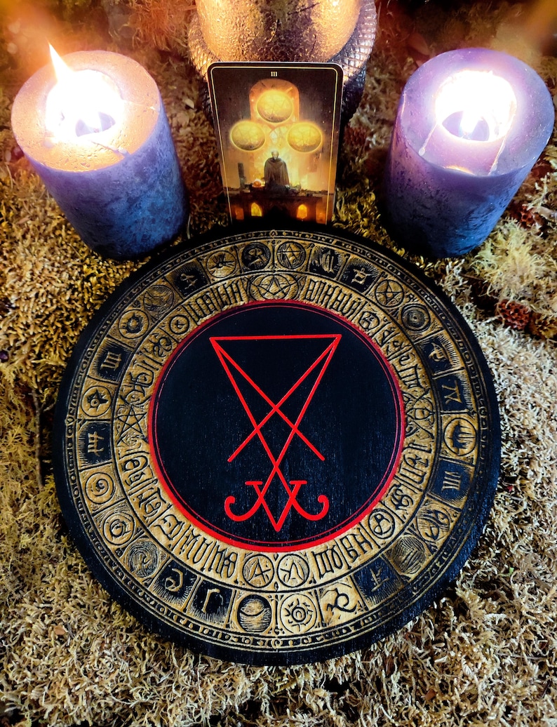 Peut inclure: Un cercle en bois noir avec un pentagramme rouge au centre. Le cercle est entouré d'une bande dorée avec divers symboles et glyphes. Deux bougies allumées sont en arrière-plan.