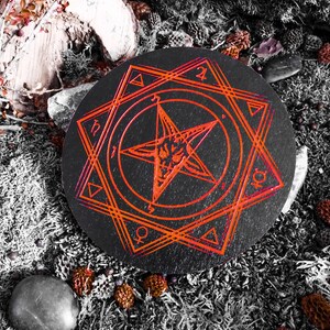 Pu&ograve; includere: Un vassoio circolare in legno nero con un design a pentagramma rosso. Il vassoio &egrave; circondato da muschio e altri elementi naturali.