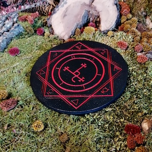 Op de afbeelding: Een zwart rond houten bord met een rood zegel en een geometrisch ontwerp. Het bord is omgeven door een rode achtpuntige ster.
