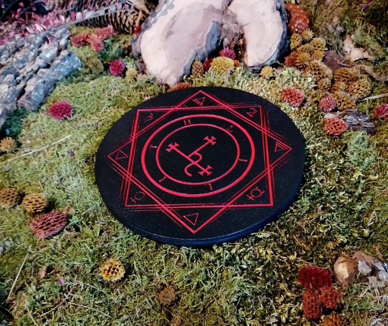 Op de afbeelding: Een zwart rond houten bord met een rood zegel en een geometrisch ontwerp. Het bord is omgeven door een rode achtpuntige ster.