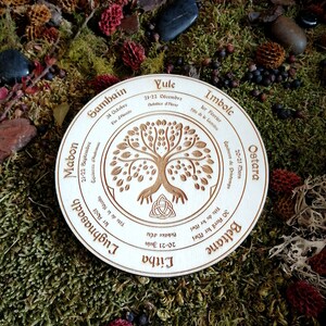 May include: A wooden circle with a tree of life design and the eight sabbats of the Wheel of the Year in French. The sabbats are Yule, Imbolc, Ostara, Beltane, Litha, Lughnasadh, Mabon, and Samhain.