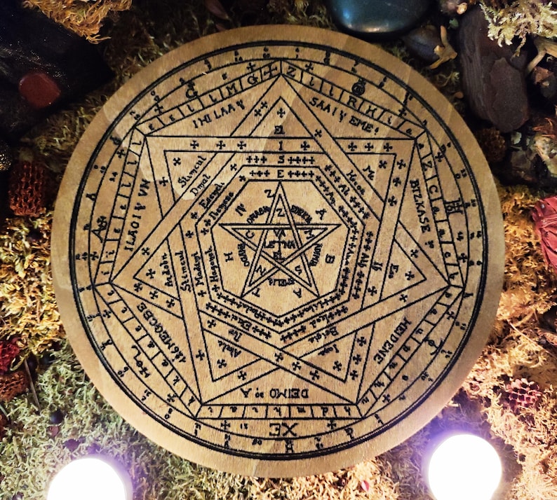 May include: A wooden circle with a black and white design of a pentagram and other symbols. The circle is surrounded by a ring of text, including the words "HEIDENE", "BIZKASE", "SAALY EME", and "ILAGIV VN".