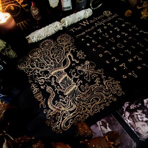 May include: A black cloth with a gold design of a tree with roots and a snake wrapped around it. The cloth also has a gold alphabet with the words "The Witches (Mage Ritual) Alphabet".