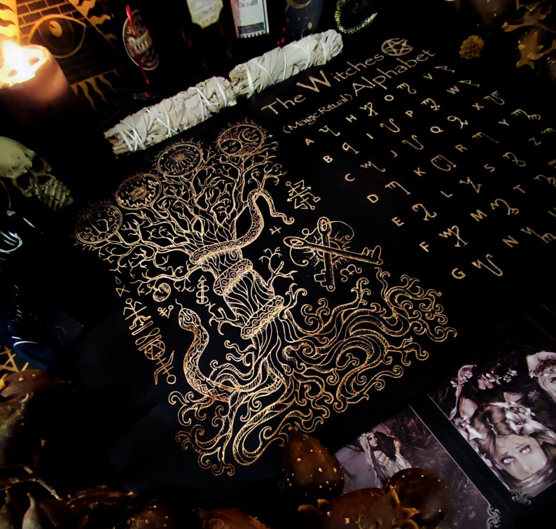 May include: A black cloth with a gold design of a tree with roots and a snake wrapped around it. The cloth also has a gold alphabet with the words "The Witches (Mage Ritual) Alphabet".