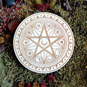 May include: A white wooden circle with a carved design of a six-pointed star with crescent moons and stars inside. The circle is surrounded by a border of stars and triangles.