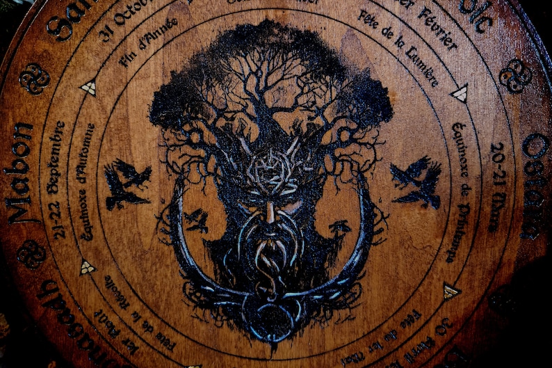 May include: A wooden circle with a tree of life design, featuring a bearded face in the centre. The circle is inscribed with text in French, including the names of the months and the equinoxes.