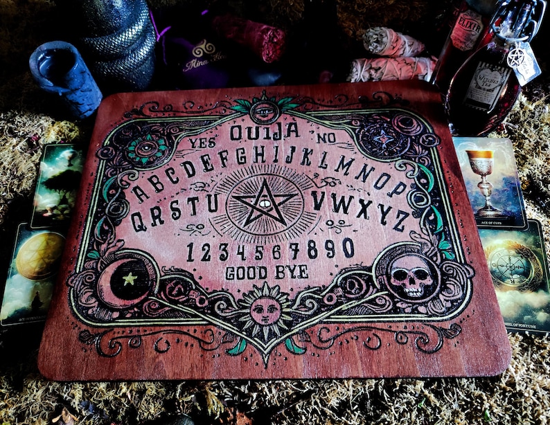 May include: A wooden Ouija board with a pink and green design. The board features a traditional alphabet, numbers, and the words "yes", "no", and "goodbye".