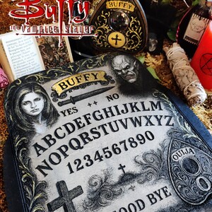 May include: A decorative Ouija board with the text "Buffy" and "Good Bye". The board features the alphabet, numbers, and a cross. Other items include a decorative heart-shaped plaque, a bottle, and a candle.