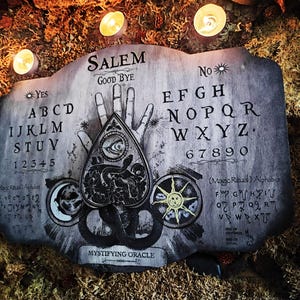 K&ouml;nnte beinhalten: Ein Ouija-Brett aus Holz mit einem schwarz-wei&szlig;en Design. Das Brett zeigt die Buchstaben des Alphabets, die Zahlen 1-9 und 0 sowie die W&ouml;rter "Ja", "Nein", "Leb wohl" und "Salem". Das Brett hat auch eine Planchette mit einem Auge und einem Schlangenmuster.
