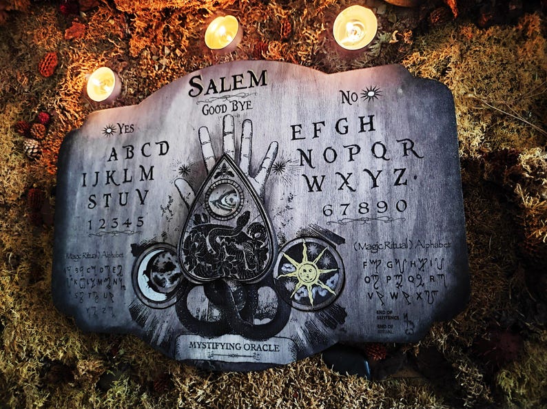 K&ouml;nnte beinhalten: Ein Ouija-Brett aus Holz mit einem schwarz-wei&szlig;en Design. Das Brett zeigt die Buchstaben des Alphabets, die Zahlen 1-9 und 0 sowie die W&ouml;rter "Ja", "Nein", "Leb wohl" und "Salem". Das Brett hat auch eine Planchette mit einem Auge und einem Schlangenmuster.