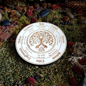 May include: A wooden circle with a tree of life design and the names of the eight sabbats of the Wheel of the Year in English and Gaelic. The sabbats are Yule, Imbolc, Ostara, Beltane, Litha, Lughnasadh, Mabon, and Samhain.