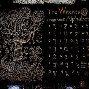 May include: A black fabric with a gold tree design and a gold alphabet with symbols. The text reads "The Witches (Magic Ritual) Alphabet".