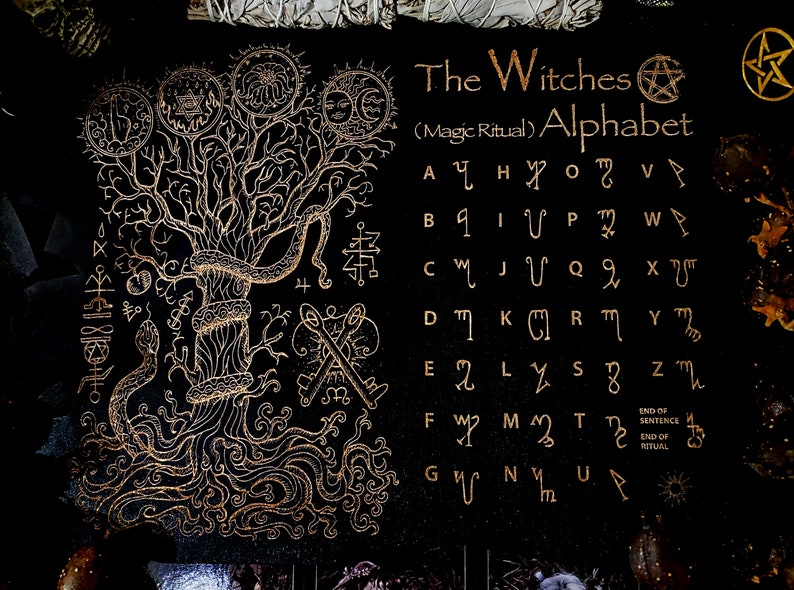 May include: A black fabric with a gold tree design and a gold alphabet with symbols. The text reads "The Witches (Magic Ritual) Alphabet".