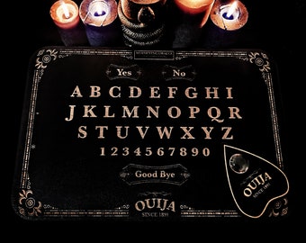 May include: A black Ouija board with gold lettering, featuring the alphabet, numbers, and the words "Yes," "No," and "Good Bye." The planchette is also black with the word "Ouija" and "Since 1891." Lit candles are in the background.