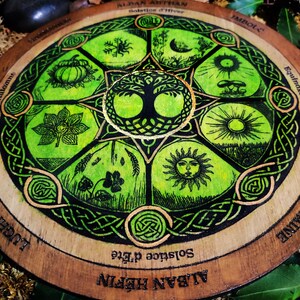 Op de afbeelding: Een houten wiel met een groen en gouden ontwerp dat de acht sabbats van het Rad van het Jaar voorstelt. Het wiel is beschreven met de woorden "Alban Hefin", "Zomerzonnewende", "Imbolc", "Nacht- en dag-equinox", "Alban Arthan", "Winterzonnewende", "Lughnasadh" en "Samhain".