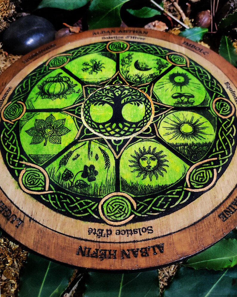 Op de afbeelding: Een houten wiel met een groen en gouden ontwerp dat de acht sabbats van het Rad van het Jaar voorstelt. Het wiel is beschreven met de woorden "Alban Hefin", "Zomerzonnewende", "Imbolc", "Nacht- en dag-equinox", "Alban Arthan", "Winterzonnewende", "Lughnasadh" en "Samhain".