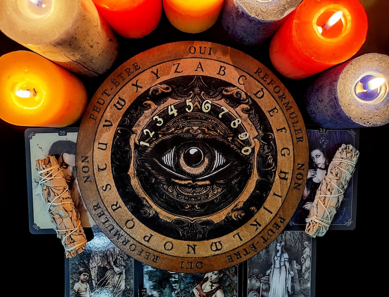 May include: A wooden Ouija board with a black and white illustration of an eye. The board has numbers 1-9 and 0, letters A-Z, and the words "Oui", "Peut-&ecirc;tre", "Non", and "Reformuler".