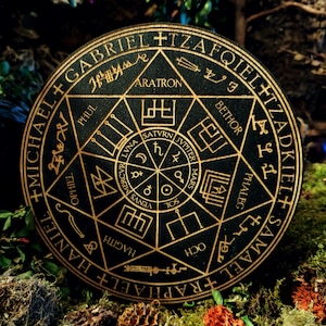 Peut inclure: Un cercle en bois noir avec des lettres et des symboles dorés. Le cercle présente les noms d'anges, dont Michael, Raphaël et Samaël, ainsi que les noms des planètes et des symboles astrologiques. Le texte indique " +MICHAEL+RAPHAEL+HANIEL+SAMAEL+TZADKIEL+TZAFQIELET+GABRIEL+ARATRON+BETHOR+PHALEG+OCH+HAGITH+PHUL+OPHIE+VENUS+MERCVRI+LVNA+SATVRN+JVPITER+MARS+SOL ".