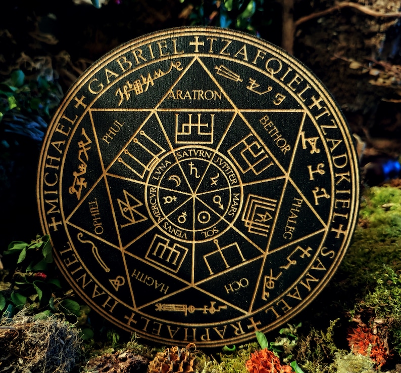 K&ouml;nnte beinhalten: Ein schwarzer Holzkreis mit goldenen Schriftz&uuml;gen und Symbolen. Der Kreis zeigt die Namen von Engeln, darunter Michael, Raphael und Samael, sowie die Namen von Planeten und astrologische Symbole. Der Text lautet " +MICHAEL+RAPHAEL+HANIEL+SAMAEL+TZADKIEL+TZAFQIELET+GABRIEL+ARATRON+BETHOR+PHALEG+OCH+HAGITH+PHUL+OPHIE+VENUS+MERCVRI+LVNA+SATVRN+JVPITER+MARS+SOL ".
