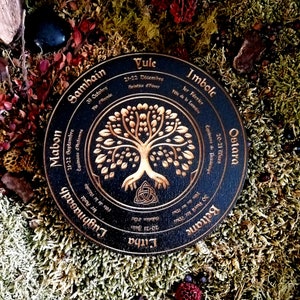 May include: A black wooden wheel with gold lettering and a gold tree design. The wheel is divided into eight sections, each representing a different time of year in the Celtic calendar. The text includes the names of the eight festivals: Yule, Imbolc, Ostara, Beltane, Litha, Lughnasadh, Mabon, and Samhain.