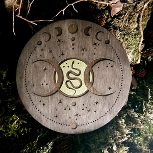 May include: A wooden circle with a triple moon design and a snake in the center. The circle is decorated with stars and moons.