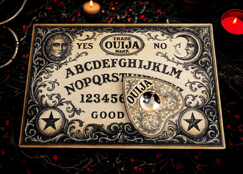 May include: A vintage Ouija board with a planchette. The board features the alphabet, numbers, and the words "Yes," "No," and "Good." Decorative elements include a sun, moon, stars, and ornate scrollwork. The planchette has the word "Ouija" on it.