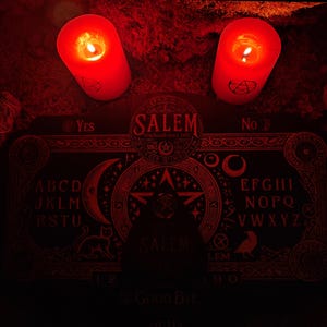 May include: A red Ouija board with the word "SALEM" in a circle in the center. The board is surrounded by candles and other occult items.