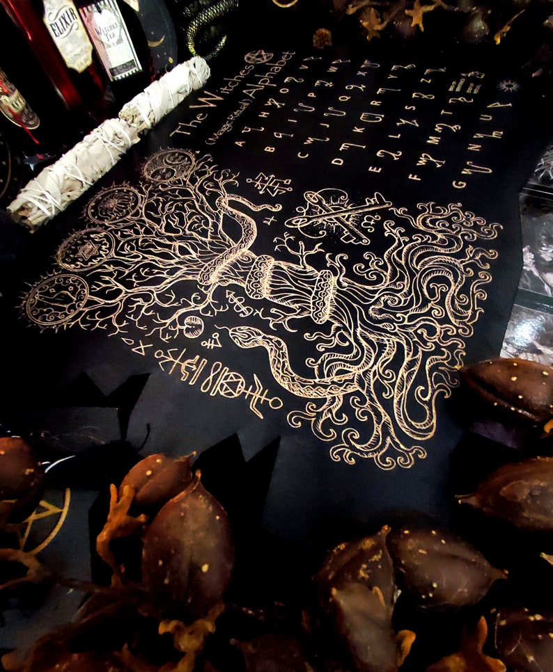 May include: A black and gold witch's alphabet chart with a tree and snake design. The chart includes the letters of the alphabet and symbols.