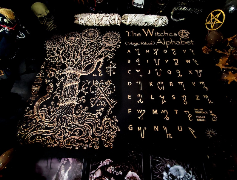 May include: A black and gold illustrated book with a tree of life design on the left page and a witches alphabet on the right page. The alphabet is written in gold and includes the text "The Witches (Magic Ritual) Alphabet".