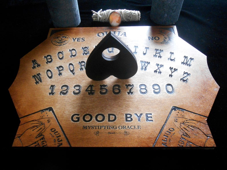 May include: Wooden Ouija board with a black heart-shaped planchette, the letters A through Z, numbers 1 through 9 and 0, and the words "YES", "NO", and "GOOD BYE".