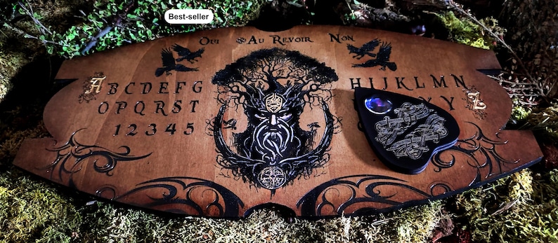 May include: Wooden Ouija board with a black and white illustration of a tree spirit with a beard. The board has a black planchette with a glass lens and the letters of the alphabet, numbers 1-9, and the words "Oui", "Au Revoir", and "Non".