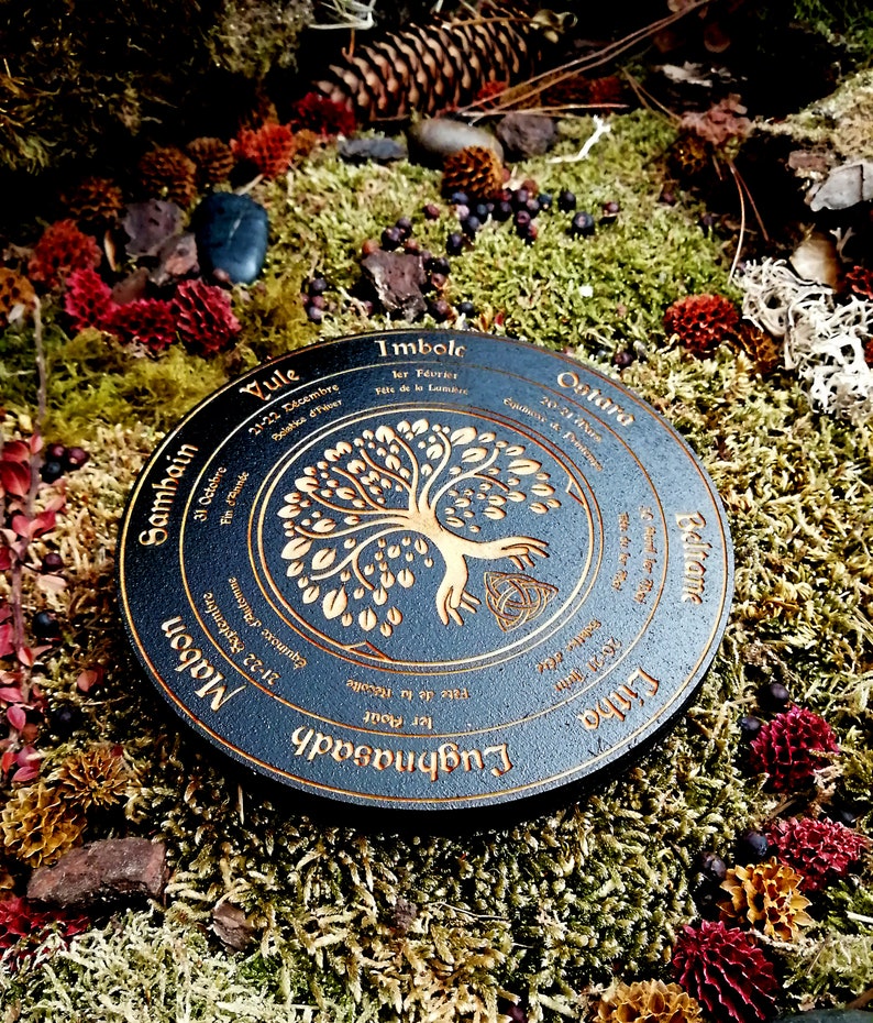 May include: A black wooden wheel with gold lettering and a tree of life design. The wheel is divided into eight sections, each representing a different time of year in the Celtic calendar. The text on the wheel includes the names of the eight festivals: Yule, Samhain, Mabon, Lughnasadh, Litha, Ostara, Imbolc, and Beltane.
