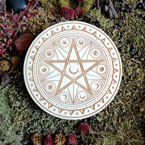May include: A wooden circle with a carved design of a six-pointed star surrounded by a circle of crescent moons. The circle is on a bed of green moss with small red and brown berries.